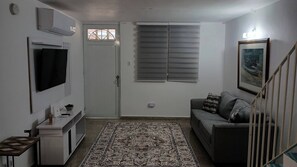 Een woonkamer met een bank, een televisie, een kamerbreed tapijt en een trap.