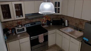 Een kleine keuken met een kookplaat, oven, broodrooster, spoelbak en kastjes.