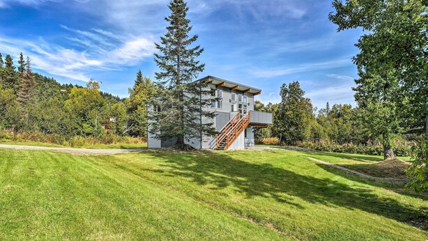 A modern two-story house with a wooden staircase, surrounded by a well-maintained lawn and tall trees. - Steps to Fritz Creek! 2-Unit Family Retreat (Fritz Creek)