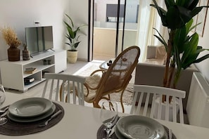 Ein Essbereich mit einem weißen Tisch für zwei Personen, einem Fernsehgerät auf einem weißen Schrank und Topfpflanzen.