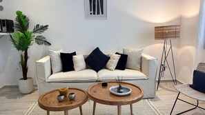 Ein Wohnzimmer mit einer Couch, zwei kleinen Tischen, einer Stehlampe und einem Blumentopf.