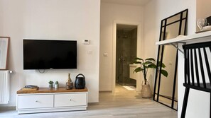 Ein modernes Wohnzimmer mit Flachbildfernseher, einem weißen Schrank, einem Blumentopf und einer Glasduschtür.