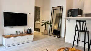 Ein modernes Wohnzimmer mit Flachbildfernseher, einer Holzkonsole, einer Topfpflanze, einem Spiegel und einer Bar mit einem Weinglas und einem schwarzen Sessel.