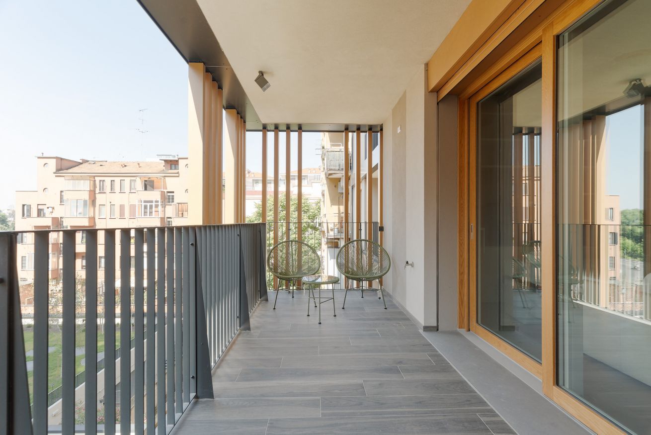 A balcony with a view of neighboring buildings, a table with chairs, and a glass door.