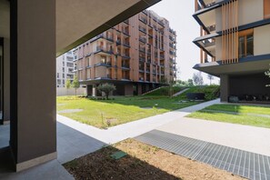Ein modernes Apartmenthaus mit mehreren Balkonen, einem gepflasterten Innenhof und einem kleinen Garten.