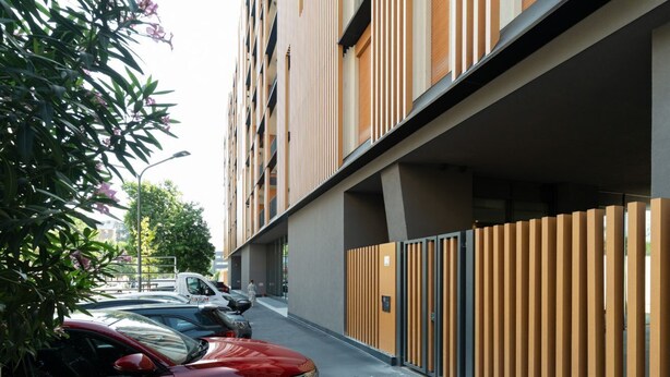 Um edifício moderno com área de estacionamento coberta e um carro vermelho estacionado na frente.