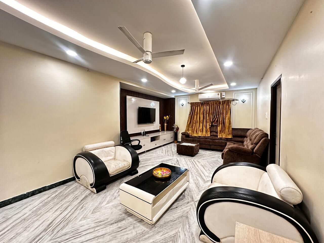 A modern living room with a flat-screen TV, two sofas, a coffee table, and ceiling fans.