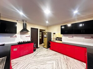 A kitchen with red cabinets, a black stove, and a refrigerator with a cartoon character. - Spacious 5-bedroom bungalow in gorgeous Chennai with AC (Chennai)