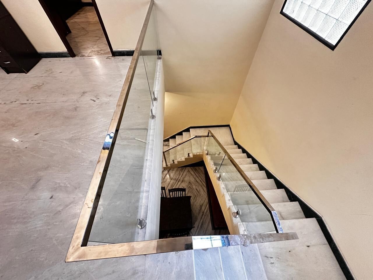 A staircase with a glass railing, marble steps, and a view of a lower level.