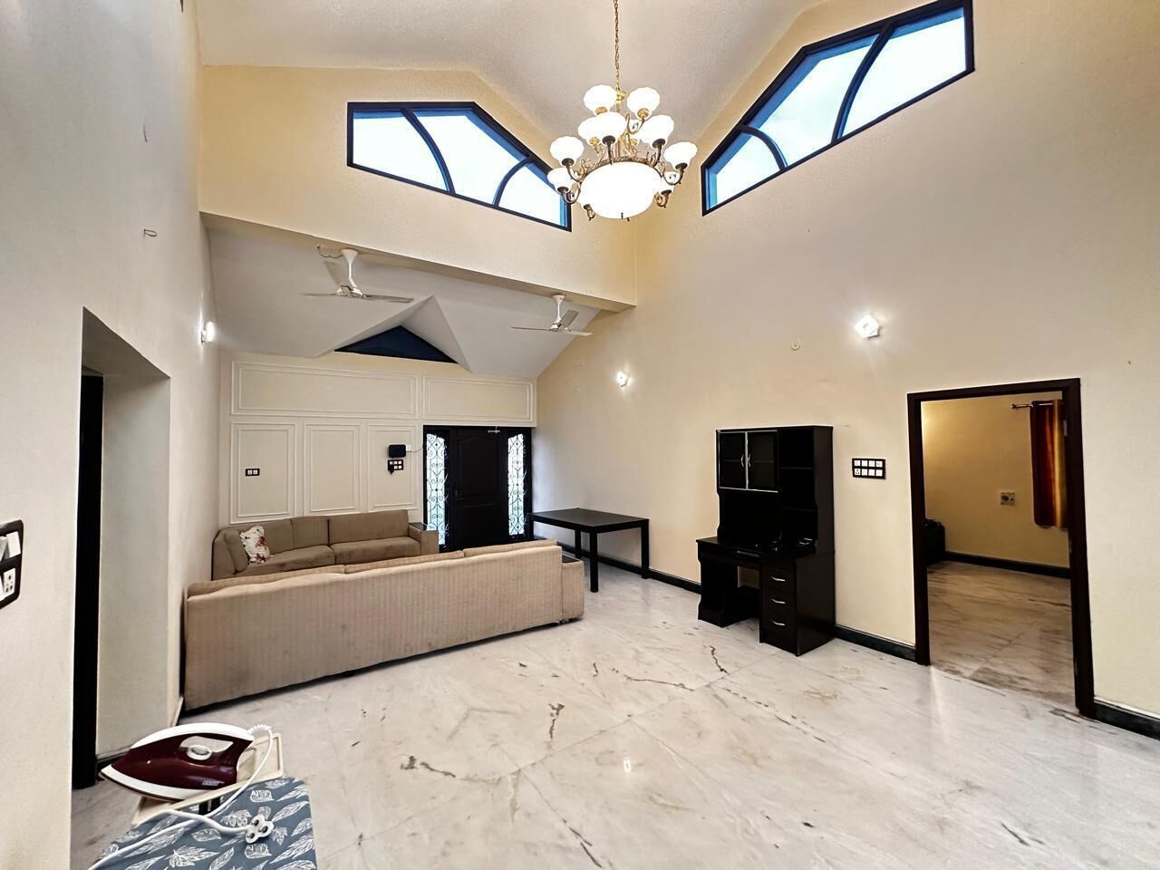 A spacious living area with a sofa, a television, and a chandelier. There are skylights and a ceiling fan.