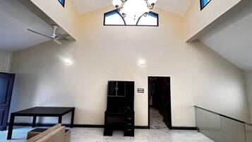 A spacious room with a ceiling fan, a black desk, a cushioned bench, and a staircase leading to another level.