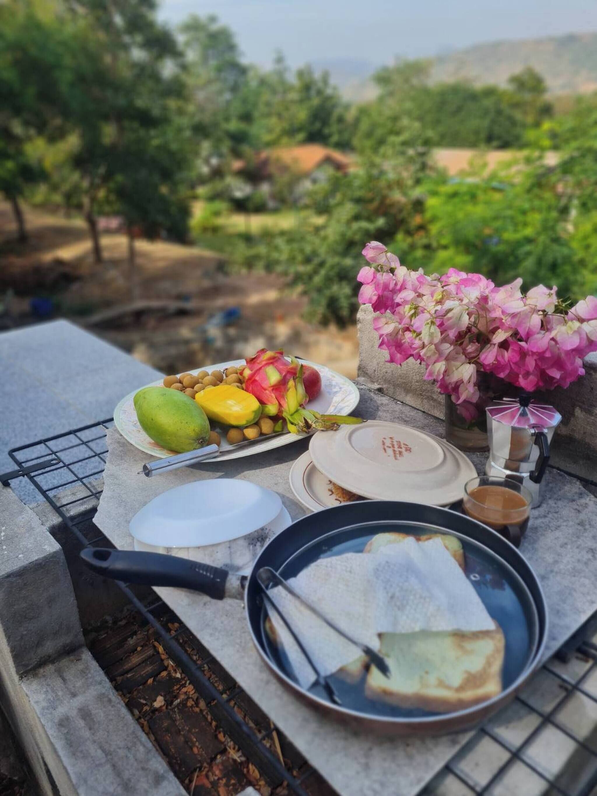 Une table dressée à l’extérieur, avec des fruits, des fleurs et une cafetière.
