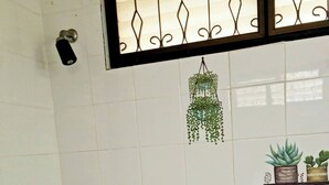 Un baño con paredes de azulejos blancos, una planta colgante, un dispensador de jabón y un pequeño estante con plantas en macetas.