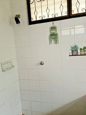 Un baño con paredes de azulejos blancos, una planta colgante, un dispensador de jabón y un pequeño estante con plantas en macetas.