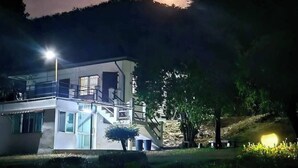 Un edificio moderno con un balcón, rodeado de árboles y una colina al fondo.