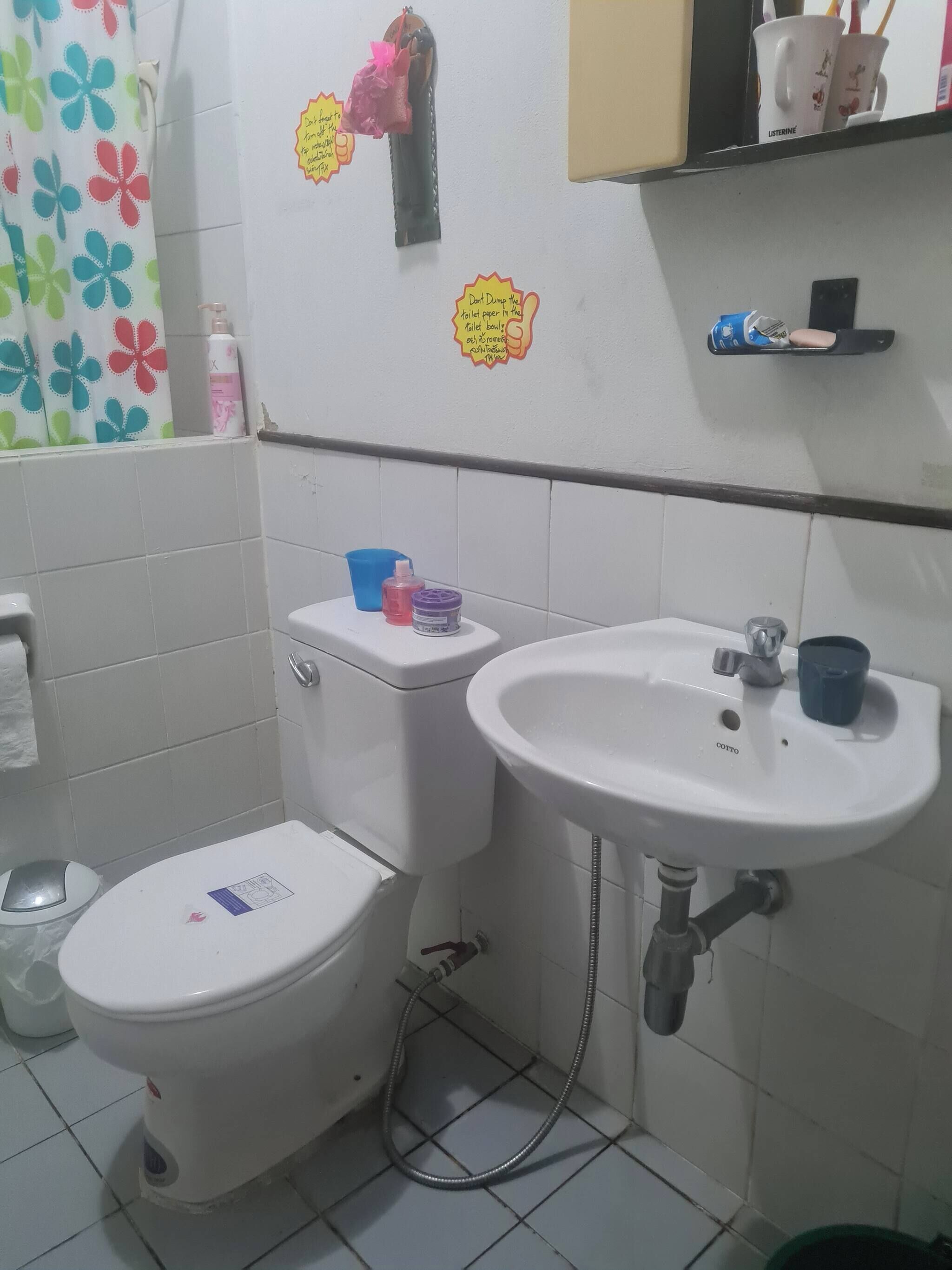 Une salle de bain avec des toilettes, un lavabo et une douche. Il y a des autocollants sur le mur, un porte-serviettes et une étagère avec divers objets.