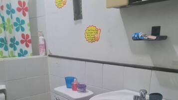 Une salle de bain avec des toilettes, un lavabo et une douche. Il y a des autocollants sur le mur, un porte-serviettes et une étagère avec divers objets.