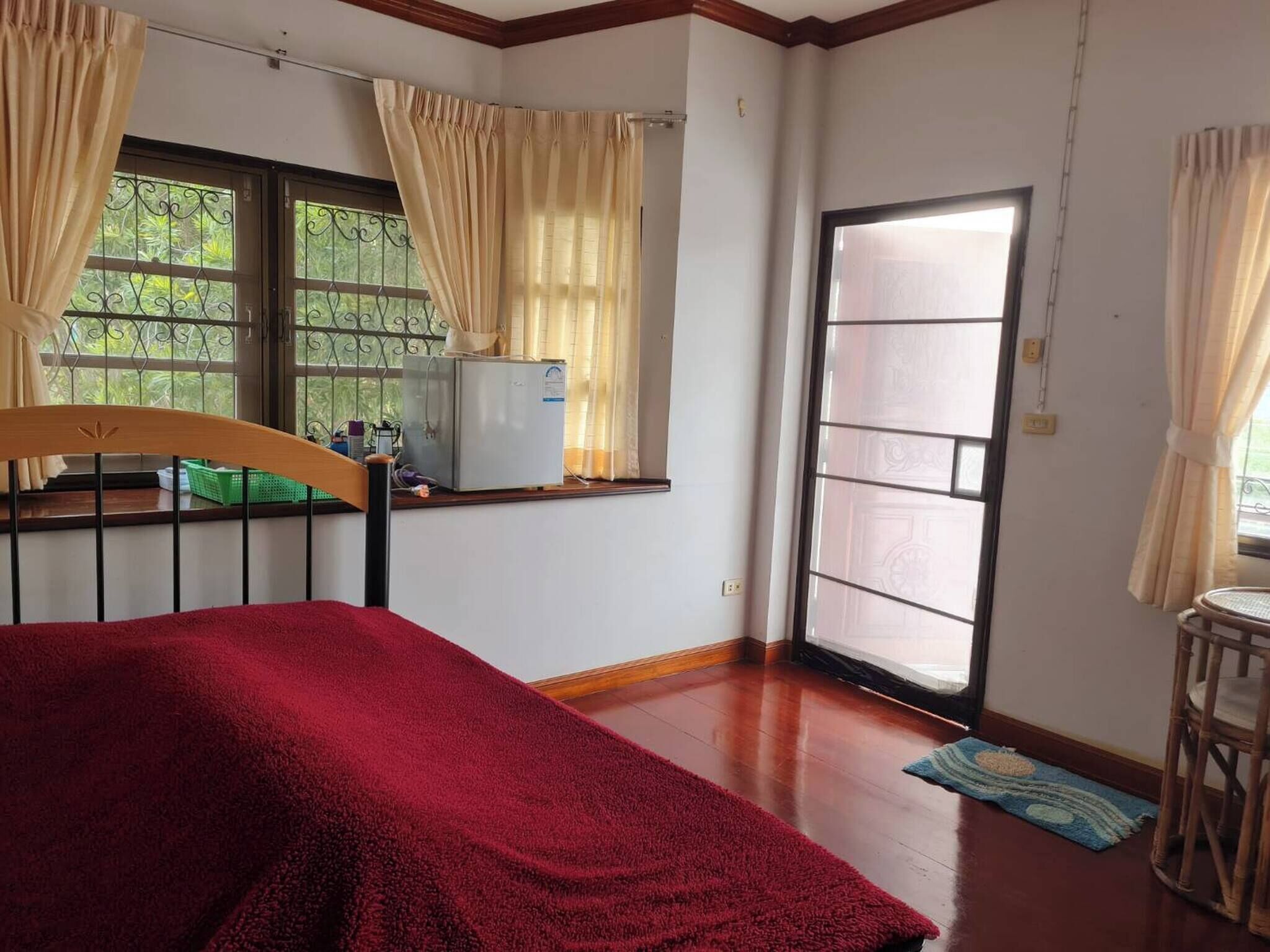 A bedroom with a bed, a window with curtains, a small table, and a door leading outside.
