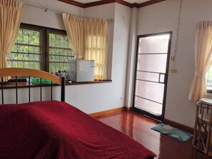 Un dormitorio con cama, una ventana con cortinas, una mesita y una puerta que da al exterior.
