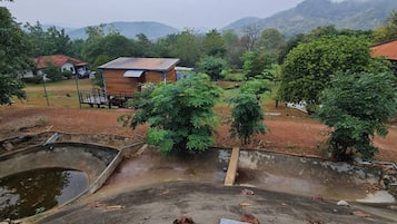 A black dog lying on a tiled surface with a view of a rural landscape, including a wooden building and a pond.
