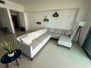 Ein Wohnzimmer mit einer L-förmigen Eckcouch, einem kleinen runden Tisch mit einem Blumentopf und einer Stehlampe.