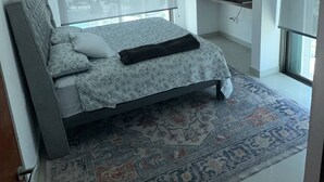 Ett sovrum med en säng, en tv, ett fönster med persienner och en mönstrad matta.