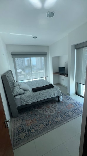 Ein Schlafzimmer mit einem Bett, einem Fernseher, einem Fenster mit Jalousien und einem gemusterten Teppich.
