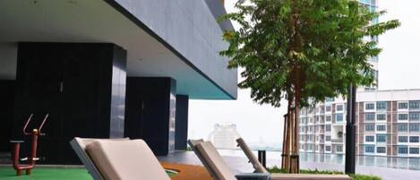 A rooftop lounge area with sun loungers, a small exercise area, and a tree.
