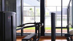 Una palestra con attrezzature per esercizi e ampie finestre che danno su un edificio.