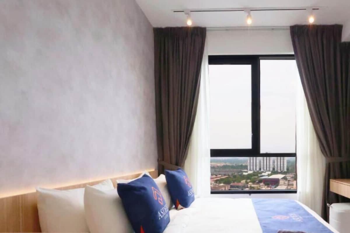 Ein Hotelzimmer mit Bett, Nachttisch, Fenster mit Vorhängen und Blick auf die Stadt.