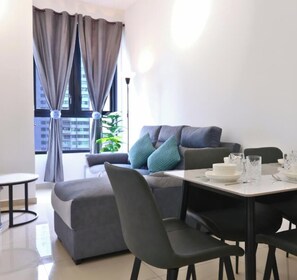 Ein modernes Wohnzimmer mit einem grauen Sofa, einem Esstisch mit Stühlen und einem Fenster mit Vorhängen.