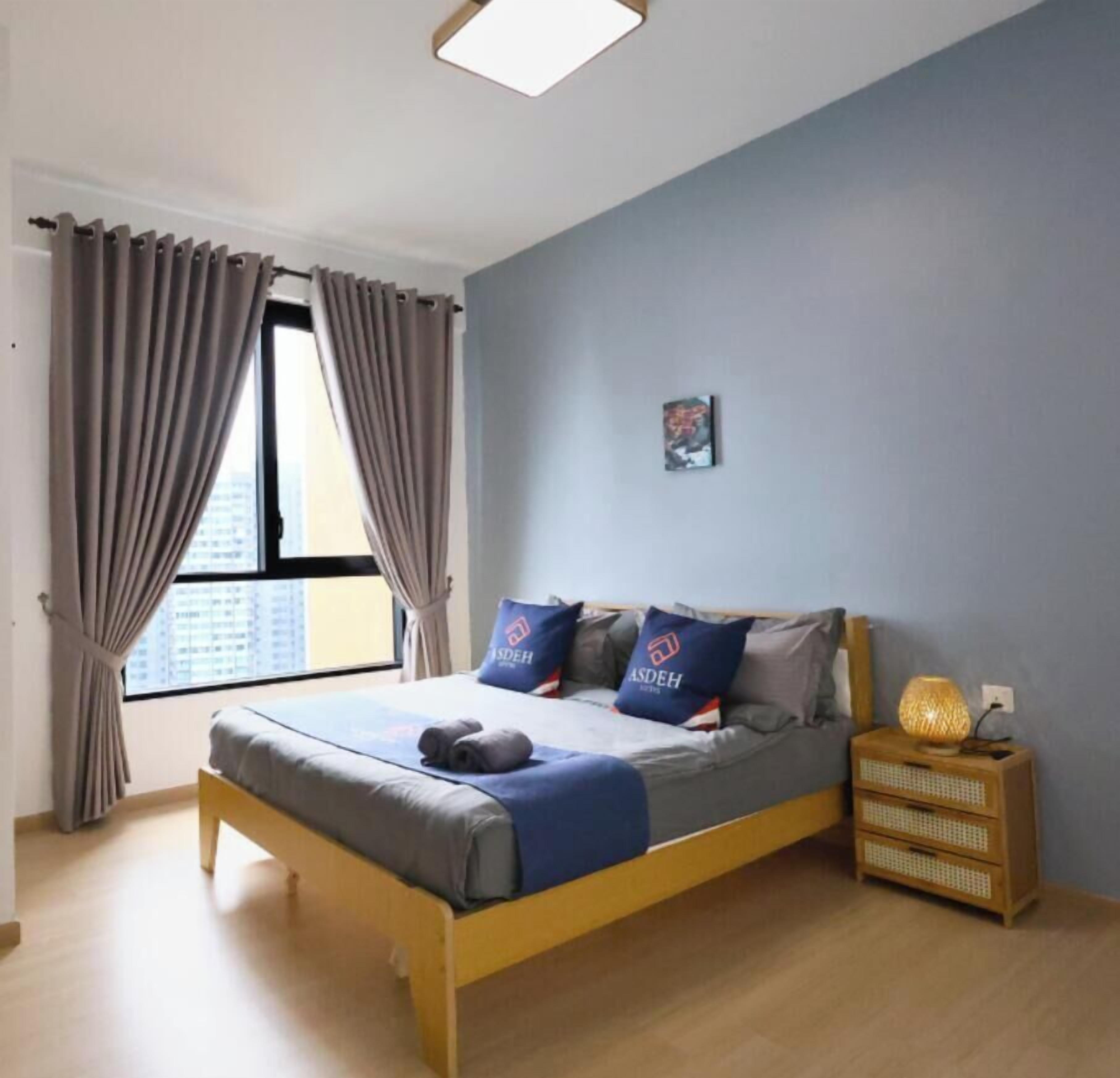 A bedroom with a bed, curtains, a bedside table with a lamp, and a wall-mounted picture.