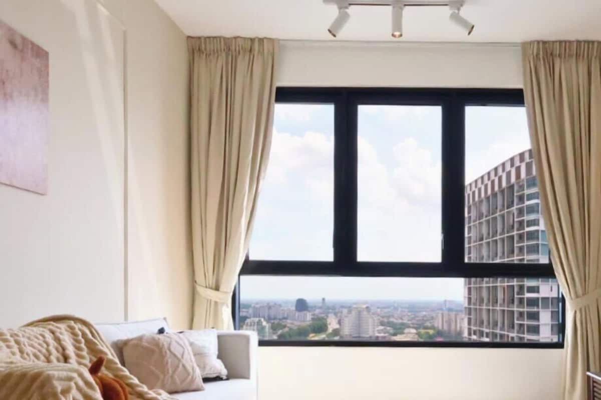Ein modernes Wohnzimmer mit großem Fenster, einer Couch, einem runden Couchtisch und Blick auf eine Stadtlandschaft.