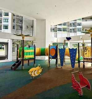A children's play area with various play structures, including slides and climbing frames, in a modern building with large windows and balconies. - I-City Shah Alam Residences By Asdeh (Shah Alam)