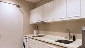A compact kitchen with white cabinets, a washing machine, a sink, and a countertop. - I-City Shah Alam Residences By Asdeh (Shah Alam)