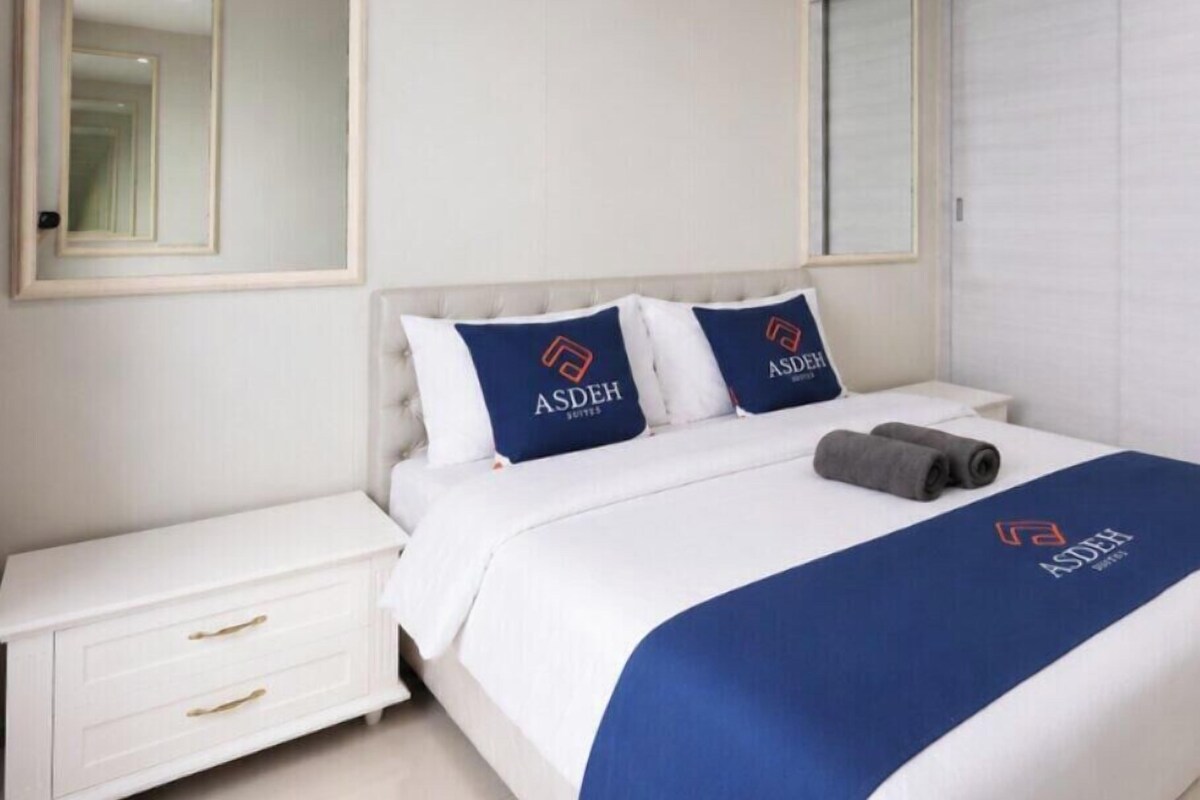 Ein Hotelzimmer mit einem Bett, einem Nachttisch, einem Spiegel und einem Fenster mit Jalousien.