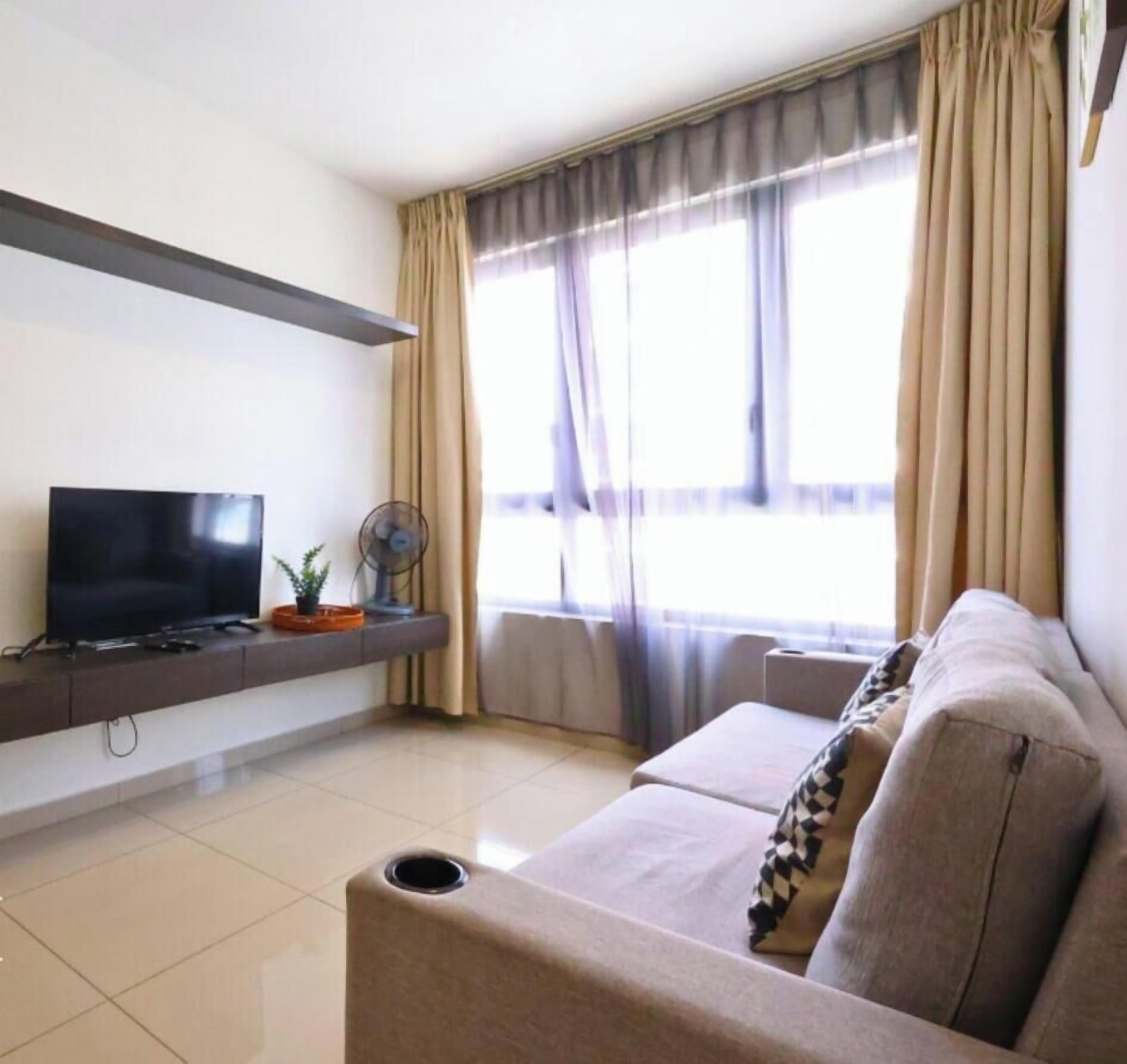 A living room with a flat-screen TV, a sofa, a fan, and a window with curtains.