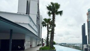 A rooftop pool with a clear view of the city skyline, a modern building with a flat roof, and a palm tree. - I-City Shah Alam Residences By Asdeh (Shah Alam)