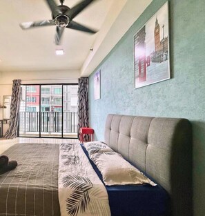 A hotel room with a bed, a ceiling fan, a window with a view of buildings, and a red stool. - I-City Shah Alam Residences By Asdeh (Shah Alam)