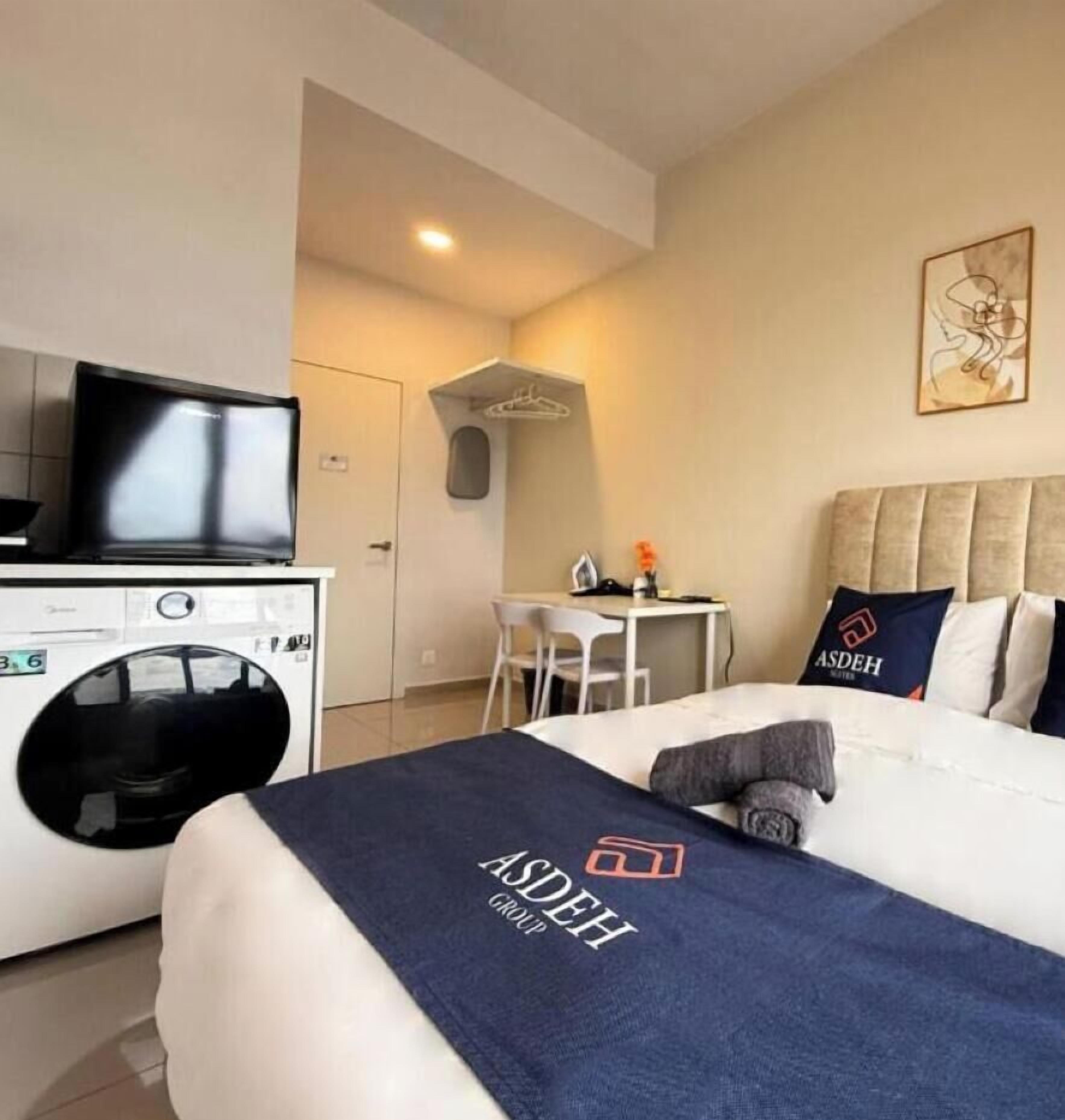 A hotel room with a bed, a desk, a washing machine, and a television.