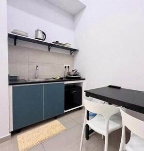 A compact kitchen with a black countertop, white chairs, and a small table. - Midlands City Broga Semenyih By Asdeh Suites (Semenyih)