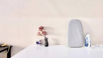 A white countertop with a blue cabinet below, a white cushion, a vase with pink flowers, and an iron on the right side.
