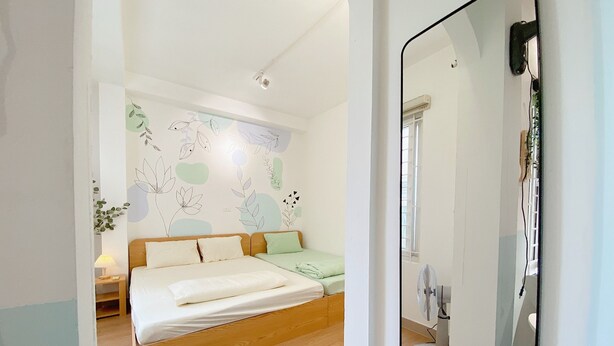 A bedroom with a wooden bed, a green pillow, a wall with abstract floral designs, and a white ceiling. - Fun 1BR w/Games, Budget Stay in Hanoi Old Quarter, Max 4, Locker, Free Wash (Hà Nội)
