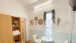 A room with a wooden wardrobe, a small table with two chairs, a window with a view, and a wall-mounted fan. - Fun 1BR w/Games, Budget Stay in Hanoi Old Quarter, Max 4, Locker, Free Wash (Hà Nội)