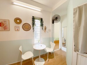 A room with a round table, two white chairs, a window with a view, and a fan on the wall. - Fun 1BR w/Games, Budget Stay in Hanoi Old Quarter, Max 4, Locker, Free Wash (Hà Nội)