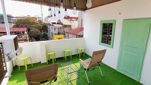 A balcony with green artificial grass, a metal grill table, two brown chairs, and a green door. - Fun 1BR w/Games, Budget Stay in Hanoi Old Quarter, Max 4, Locker, Free Wash (Hà Nội)