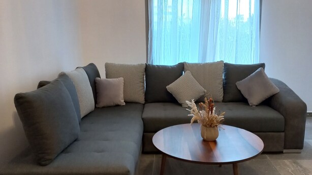 Ein modernes Wohnzimmer mit einem Ecksofa, einem runden Couchtisch und einer Vase mit getrockneten Blumen.