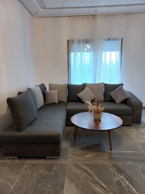 A modern living room with a sectional sofa, a round coffee table, and a vase of dried flowers. - Beachfront Apartment (Sidi rahal Chatai)
