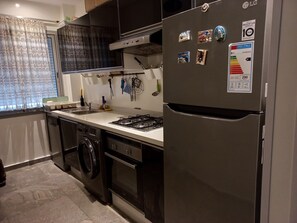 Eine kompakte Küche mit einem Edelstahl-Kühlschrank, einem Gasherd, einem Backofen und einer Waschmaschine.