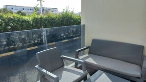 Ein Balkon mit einer Sitzecke aus einer Bank und zwei Stühlen, einer Glastrennwand und Blick auf eine Straße sowie auf Gebäude.